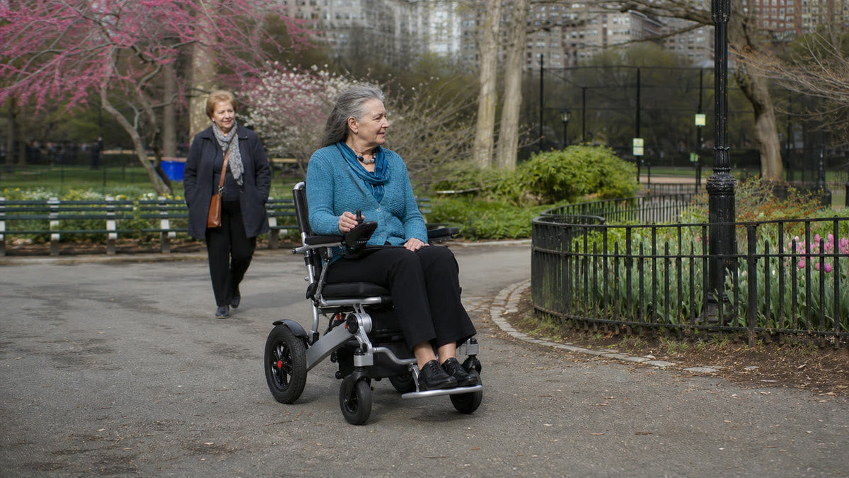 Fictional older adult using the Anywell YA12-5 on a paved park path; real-source-informed AI lifestyle scene